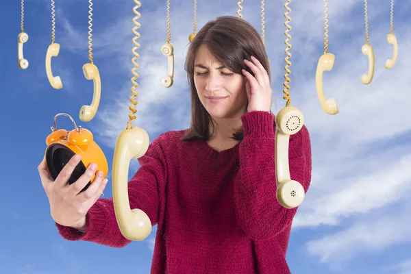 頭痛と女性の掛かる古い旧式携帯電話と持株目覚まし時計 青い空を背景立っている女性 — ストック写真