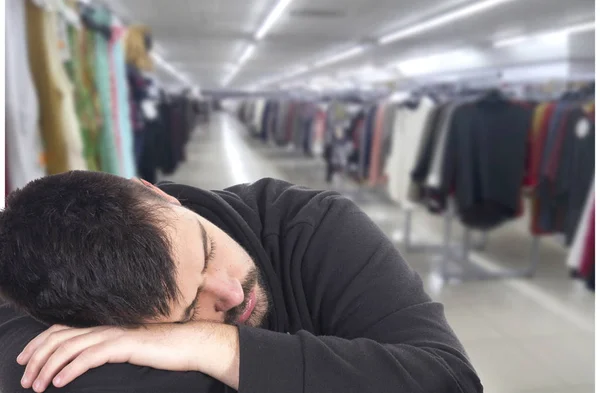 tired, sleeping man in mall, hangers with clothes on background