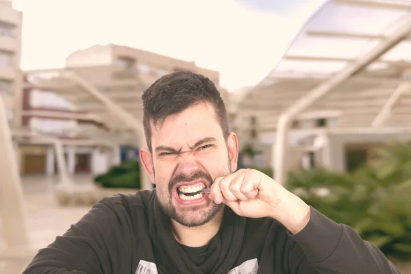 angry caucasian bearded man with pen in mouth outdoors