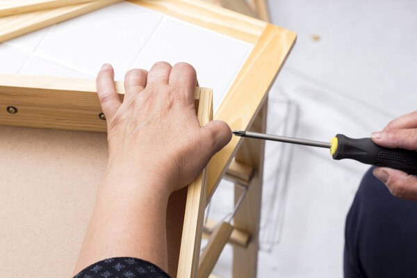 carpenter person using screwdriver tool while repairing wardrobe box