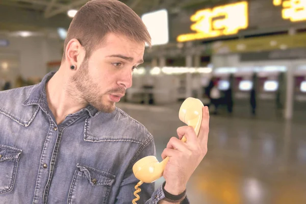 Caucasian blond man in airport terminal holding yellow old fashioned telephone