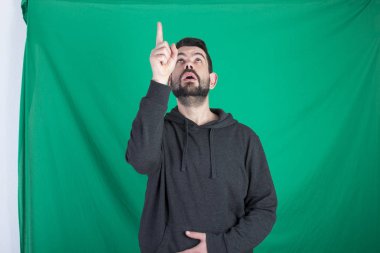 Kapüşonlu ve yeşil arka planı poz, yukarıya bakıyor ve parmak işaret adam