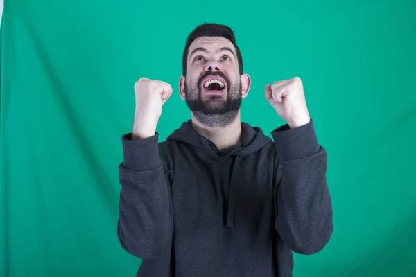 Feliz Vencedor Homem Usando Capuz Posando Contra Fundo Verde Mantendo — Fotografia de Stock