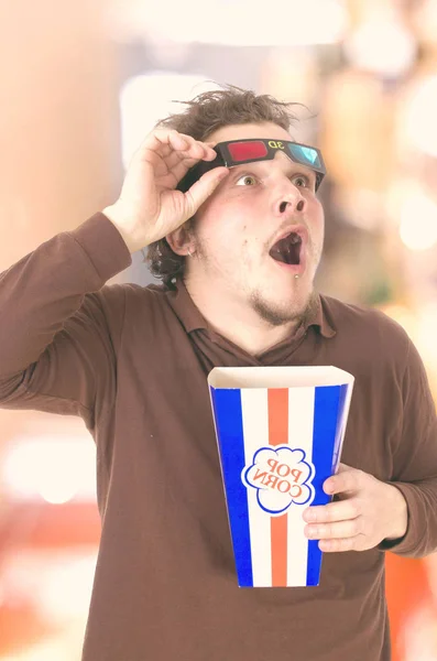 shocked man with opened mouth wearing 3D glasses and holding pop corn basket