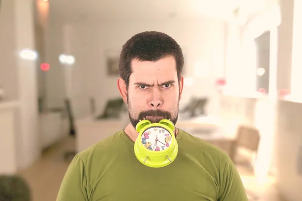 caucasian man with stubble with green alarm clock in mouth