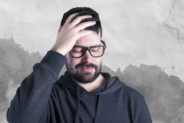 man with stubble wearing glasses and touching head with headache