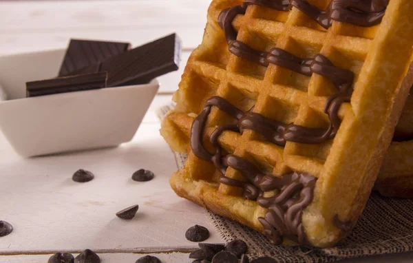 appetizing belgium waffles with chocolate syrup, chocolate slices in bowl on table