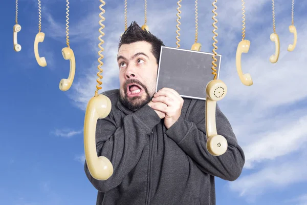 crazy man against sky surrounded by hanging old fashioned phones handsets, holding speech bubble board