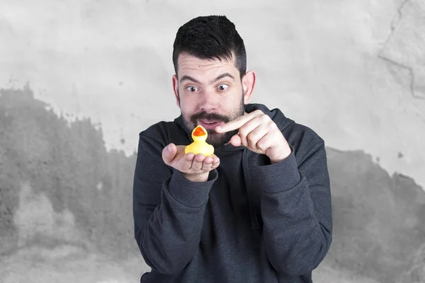 brunette man with stubble pointing finger on yellow rubber duck toy