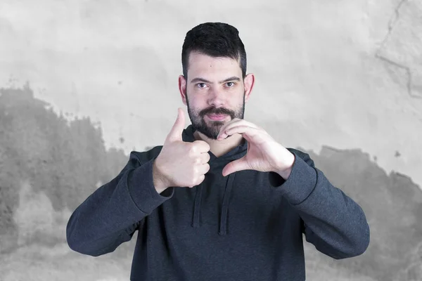 caucasian man with stubble trying to gesture heart sign with hands