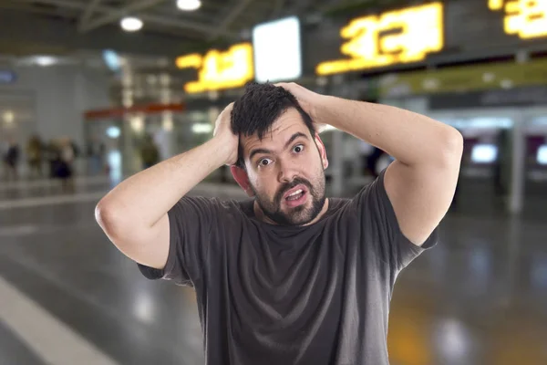 shocked man holding hands on head and looking at camera while standing airport terminal