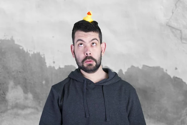 brunette man with stubble looking up on yellow rubber duck toy on head