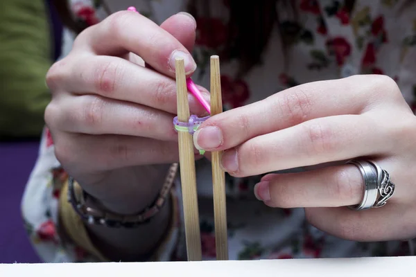 woman hands making rubber band bracelet with knitting needles, rubber bands and hook