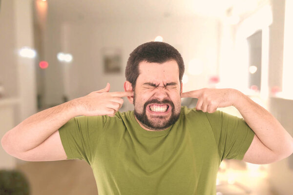 caucasian bearded man covering ears with fingers 