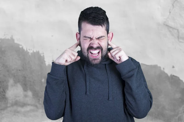 caucasian man with opened mouth, scared guy standing against grey wall and covering ears