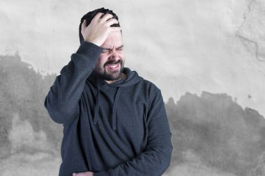 Beyaz adam ayakta gri duvar kapalı gözler ile kafasına elini tutarak karşı korkuttu 