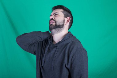 Kapüşonlu ve sırt ağrısı olan yeşil arka plana karşı poz yorgun adam 