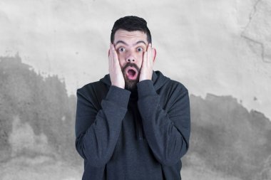 Beyaz adam açık ağızlı, korkak adam gri duvara karşı ayakta 