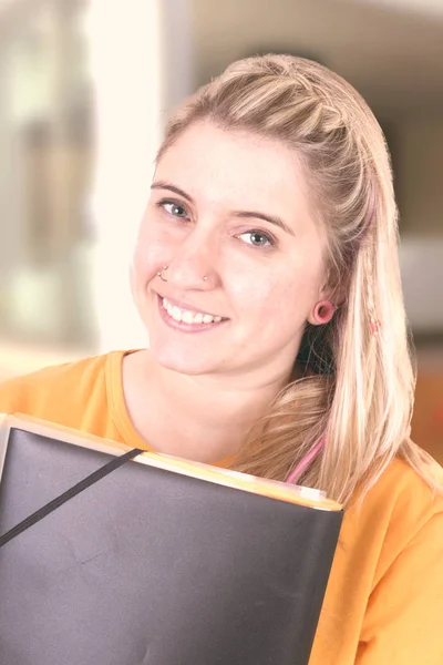 Blonde student girl holding leather folder and looking at camera