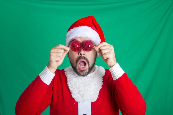 bearded man with opened mouth wearing red santa claus costume and covering eyes with Christmas balls