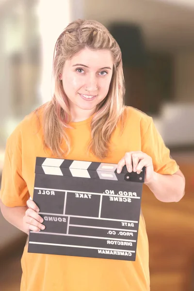 Blonde  woman with smile holding cinema clapperboard and looking at camera
