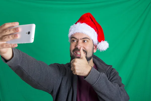 親指で携帯電話に Selfie をとる赤サンタ クロースの帽子を身に着けている幸せなひげを生やした男の笑みを浮かべてください — ストック写真