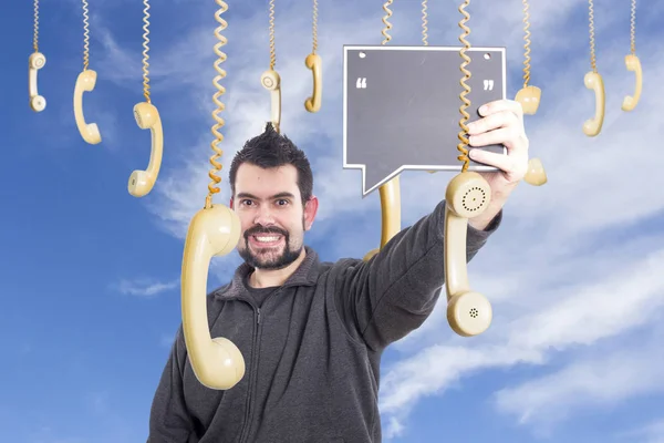 smiling man against sky surrounded by hanging old fashioned phones handsets and holding board blank