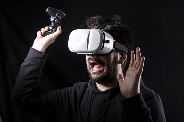 scared screaming man wearing VR glasses in darkness and holding joystick
