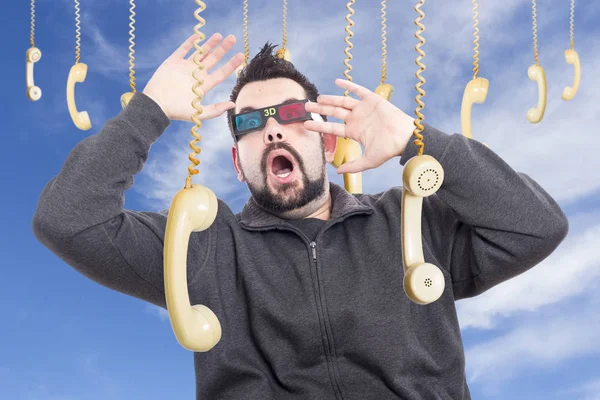 shocked man surrounded by hanging old fashioned phone handsets wearing 3-d glasses