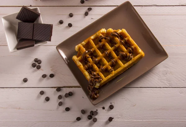 appetizing belgium waffles with chocolate syrup, chocolate slices in bowl on table