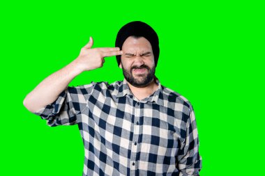 Yakın plan portresi ciddi sakallı bir adam alnında ezik işareti olan ve yeşil stüdyo arkaplanından iğrenerek sana bakan bir adam. Negatif insani duygu yüz ifadesi hissi