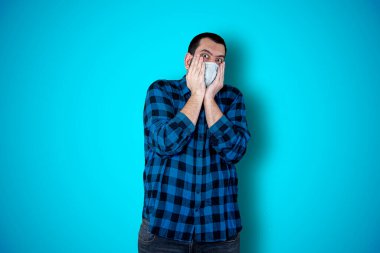 Mavi arka plan stüdyosunun üzerinde sürpriz yüz ifadesi olan bir adam. Coronavirus konsepti