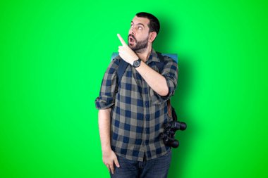 Genç gezgin adam fotokopi alanını gösteriyor ve bakıyor. Yakışıklı genç iş adamı yeşil arka planda izole edilmiş.