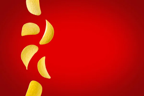 Fallende Kartoffelchips isoliert auf rotem Hintergrund. Fliegende knusprige Snacks Stockfoto
