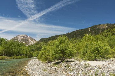 Azusa Nehri 'nin el değmemiş alp suları, Japonya' nın Kamikochi, Nagano şehrinde güneşli, mavi bir gökyüzü gününde Hotaka-Dake Dağı 'nın manzarası önünde akıyor..