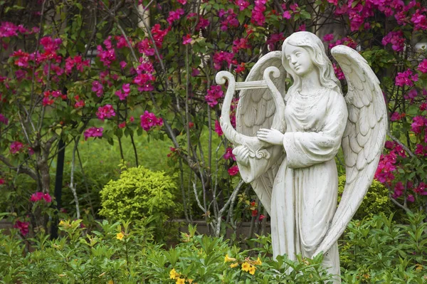 Скульптура ангела в цветочном саду — стоковое фото
