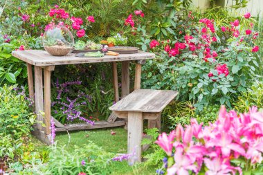 Bahçe aletleri masada ve bahar çiçekleri bahçede terasta. 