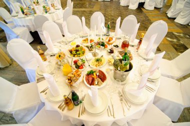 Düğün Konuklar için tablo ayarı. Parlak hall, beyaz masa örtüsü, sandalye üzerinde beyaz kapsar. Atıştırmalıklar, çatal bıçak takımı, kadehlerin, çiçekler ve masanın üzerine peçete.