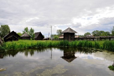 Küçük bataklık gölet köyün. Eski ahşap evler, bulrush. Bulutlu yaz gün.