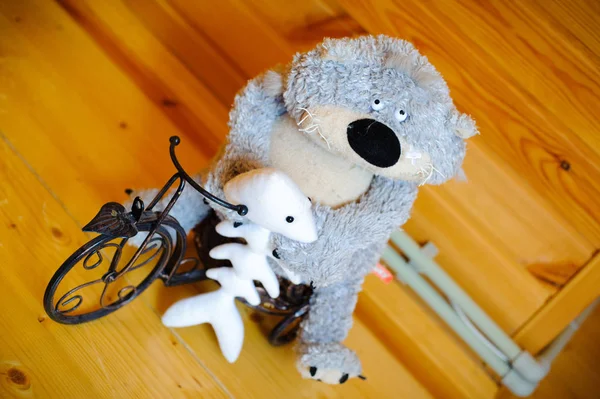 A fun little plush toy bear with fish on the toy iron bike.