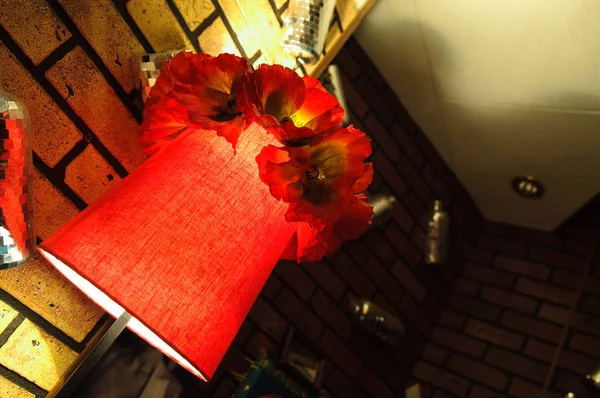 人工の花で飾られた赤い布のシェードとランプ — ストック写真