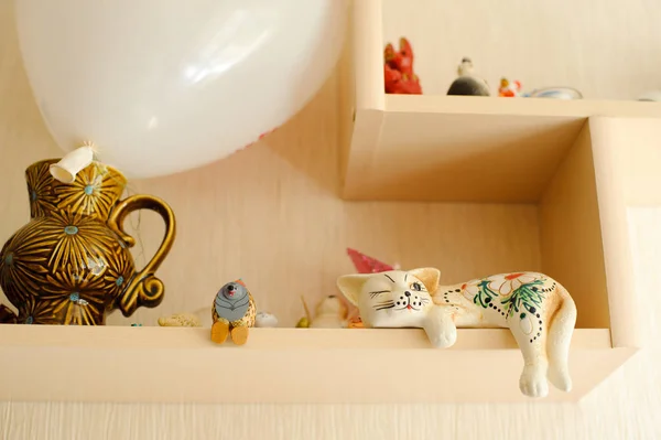 Interior of a light room. Shelf with decorative statuettes. A figurine of a cute white cat.