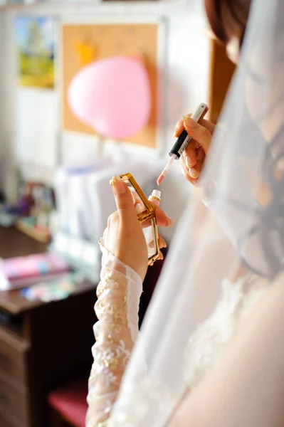 Morning preparation of the bride. The girl looks in the mirror to make up her lips.