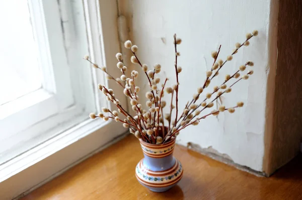 A bouquet of willow branches in a vase on the window.