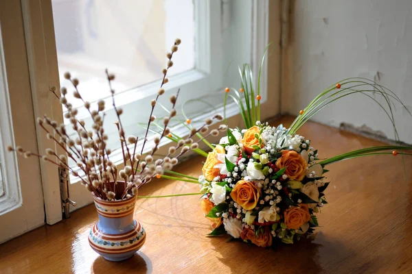 A bouquet of willow branches in a vase and a bouquet of a bride on the window.