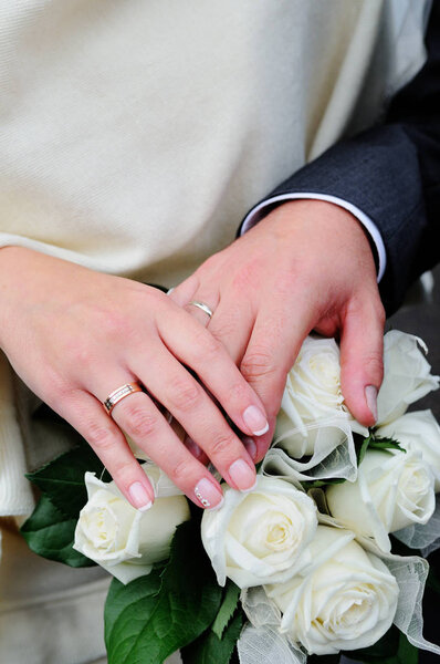 Hands of newlyweds with wedding rings on a bouquet of the bride.