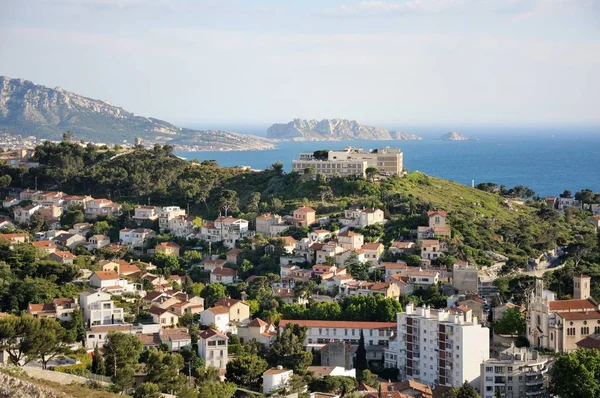 View from the height of the city on the sea coast. Small islets in the sea. Roofs of houses, trees, mountains in the background. Cloudy sky.