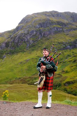 İskoçya Highlands - 24 Eylül 2015: Piper İskoçya Highlands bagpipes üzerinde geleneksel İskoç kıyafet çalış. Dağın arka planda. Bulutlu sonbahar günü.