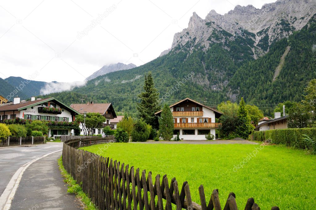 Beautiful white houses in a European village. Fresh green lawn behind the fence. Mountains in the background. Summer day.