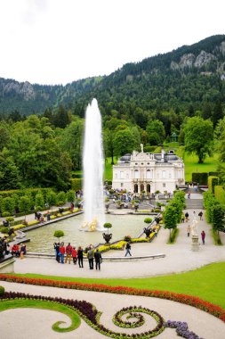 Bavyera, Almanya - 14 Ağustos 2014: Linderhof Sarayı ve park. Sarayın ana girişi. Yüksek güzel çeşme jetleri. Arka planda dağlar.